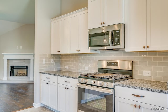 kitchen with appliances with stainless steel finishes, white cabinetry, light stone counters, and tasteful backsplash