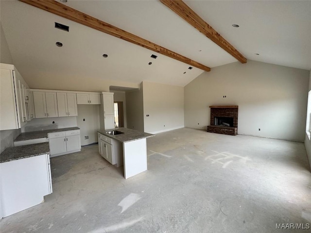 kitchen with dark countertops, open floor plan, beamed ceiling, a fireplace, and white cabinets