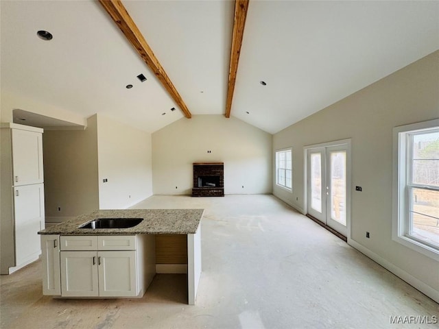 kitchen with a sink, plenty of natural light, vaulted ceiling with beams, and white cabinetry