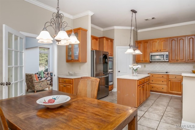 kitchen with an inviting chandelier, hanging light fixtures, ornamental molding, appliances with stainless steel finishes, and a kitchen island