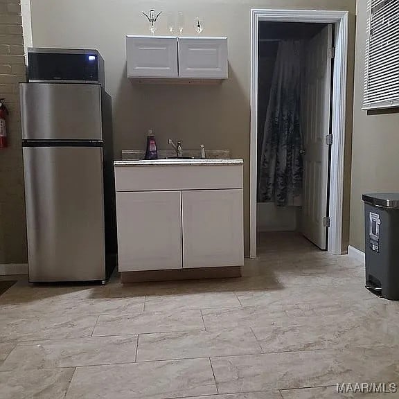 kitchen featuring white cabinetry, stainless steel refrigerator, and sink