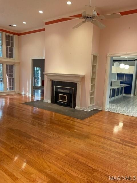 unfurnished living room with hardwood / wood-style floors, ceiling fan, crown molding, and a high ceiling