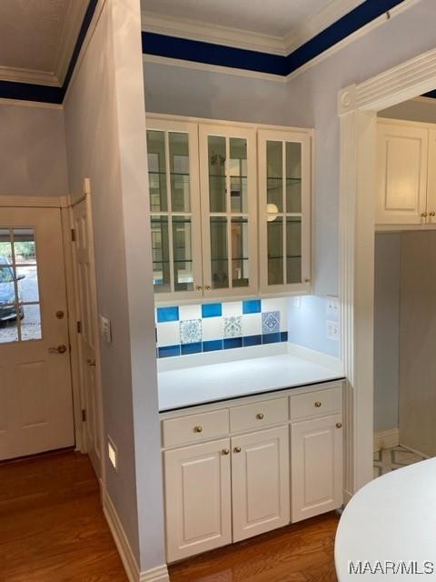 kitchen with backsplash, white cabinets, wood-type flooring, and ornamental molding