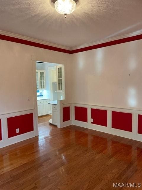 empty room featuring a textured ceiling, wood-type flooring, and ornamental molding