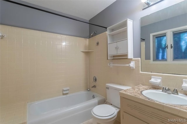 full bathroom with tiled shower / bath, vanity, toilet, and tile walls