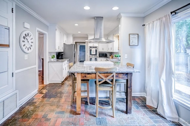 kitchen featuring light stone countertops, white cabinetry, stainless steel appliances, crown molding, and island range hood