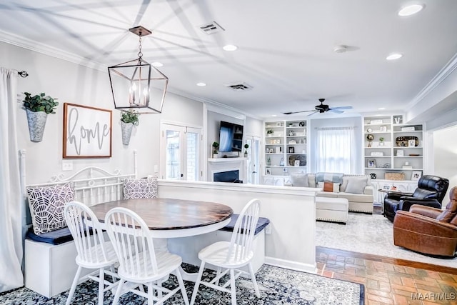 dining room featuring built in shelves, ornamental molding, and ceiling fan with notable chandelier