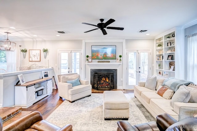 living room with a wealth of natural light, french doors, wood-type flooring, and ceiling fan with notable chandelier