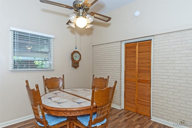 dining room featuring dark hardwood / wood-style floors, ceiling fan, and brick wall