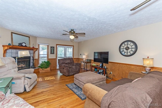 living room featuring a textured ceiling, ceiling fan, light hardwood / wood-style flooring, a fireplace, and wood walls