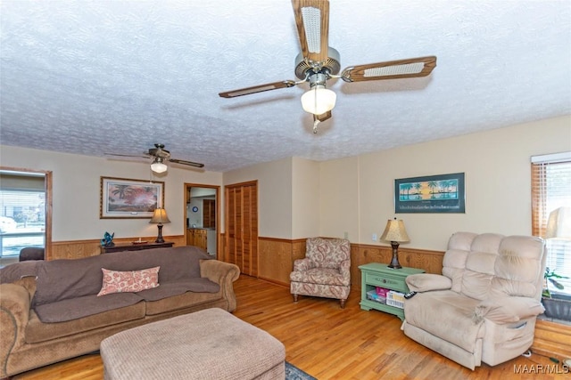 living room with wood-type flooring, a textured ceiling, ceiling fan, and wood walls