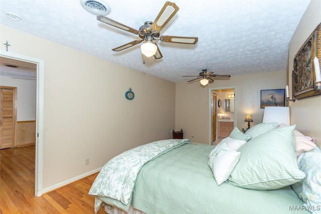 bedroom with ceiling fan, ensuite bathroom, a textured ceiling, and light wood-type flooring