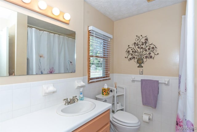 bathroom with a textured ceiling, vanity, toilet, and tile walls