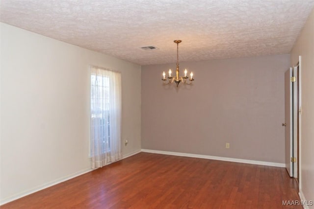 spare room featuring a chandelier, a textured ceiling, and dark hardwood / wood-style floors