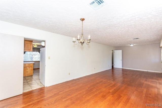 unfurnished room with light hardwood / wood-style floors, a textured ceiling, and a notable chandelier