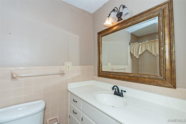 bathroom with a textured ceiling, vanity, toilet, and tile walls