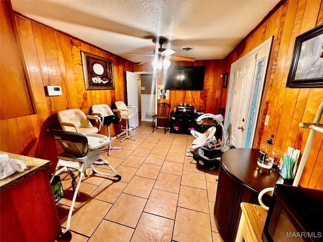 interior space featuring ceiling fan, light tile patterned floors, a textured ceiling, and wooden walls