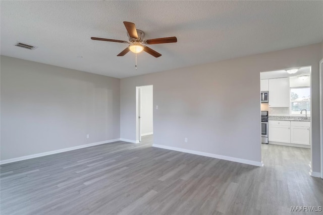 unfurnished room featuring hardwood / wood-style floors, a textured ceiling, ceiling fan, and sink