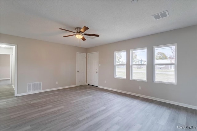 empty room with ceiling fan, light wood-type flooring, and a textured ceiling