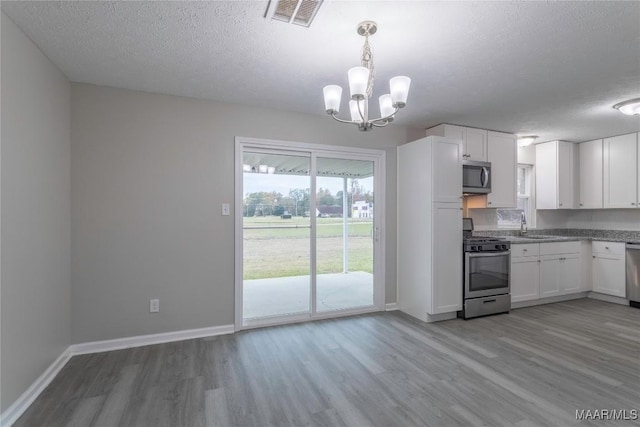 kitchen featuring appliances with stainless steel finishes, a textured ceiling, decorative light fixtures, light hardwood / wood-style flooring, and white cabinets