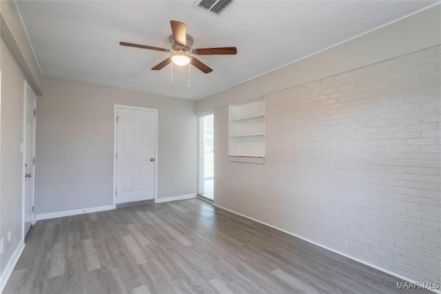 empty room with ceiling fan, wood-type flooring, and brick wall