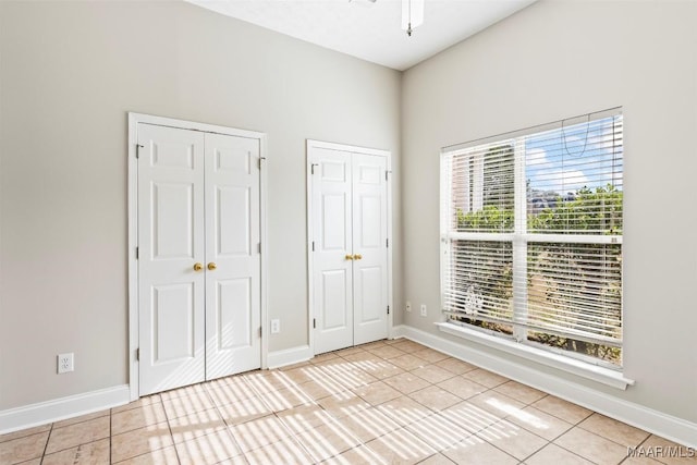 unfurnished bedroom featuring ceiling fan, light tile patterned floors, and two closets