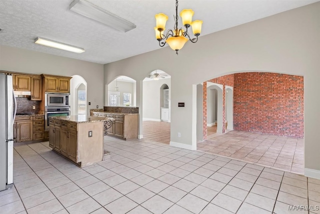 kitchen featuring ceiling fan with notable chandelier, stainless steel appliances, pendant lighting, light tile patterned floors, and a kitchen island