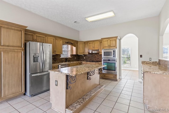 kitchen featuring backsplash, light tile patterned floors, a textured ceiling, a kitchen island, and stainless steel appliances