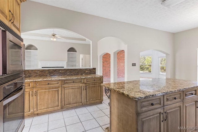 kitchen with ceiling fan, a textured ceiling, appliances with stainless steel finishes, stone countertops, and a kitchen island