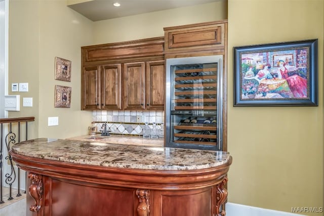 bar with light stone countertops, sink, beverage cooler, and tasteful backsplash