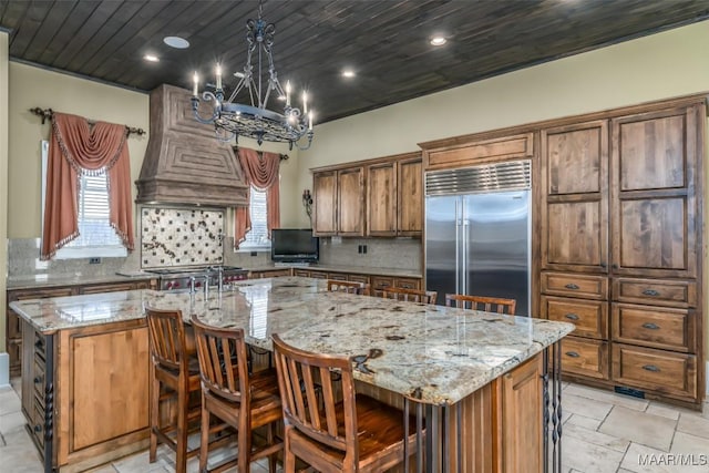 kitchen featuring a spacious island, stainless steel built in fridge, light stone countertops, and backsplash