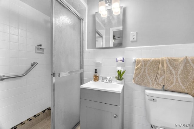 bathroom featuring a shower with door, vanity, tile walls, and toilet