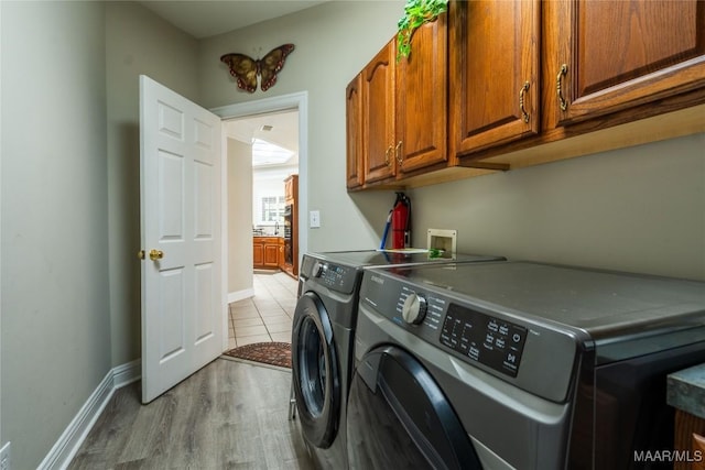 clothes washing area featuring washing machine and dryer, cabinets, and light hardwood / wood-style floors