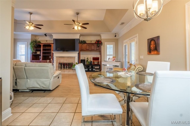 tiled dining space with ceiling fan with notable chandelier, crown molding, a tray ceiling, and a tiled fireplace