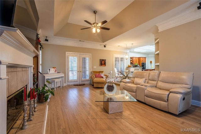 living room with french doors, a raised ceiling, ceiling fan, a tile fireplace, and light hardwood / wood-style floors