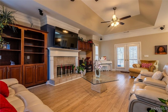 living room featuring a tile fireplace, ceiling fan, french doors, a raised ceiling, and light hardwood / wood-style floors