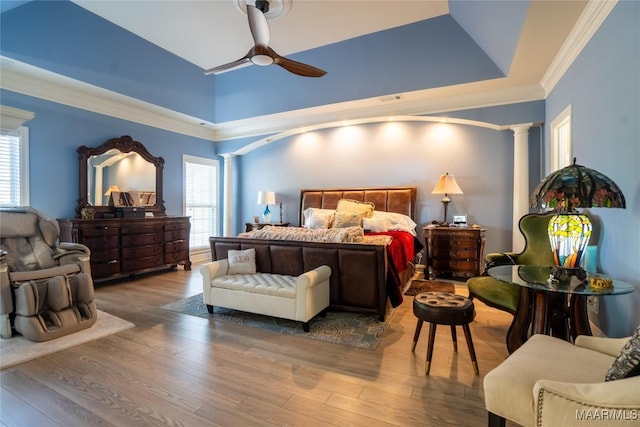 bedroom with hardwood / wood-style floors, decorative columns, ceiling fan, and a tray ceiling