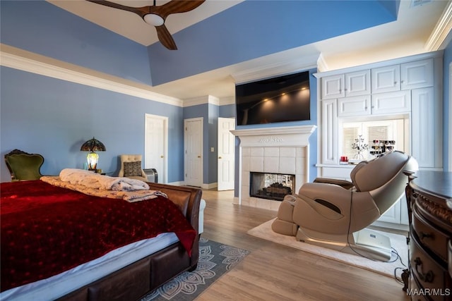 bedroom with ceiling fan, light hardwood / wood-style floors, ornamental molding, and a tiled fireplace