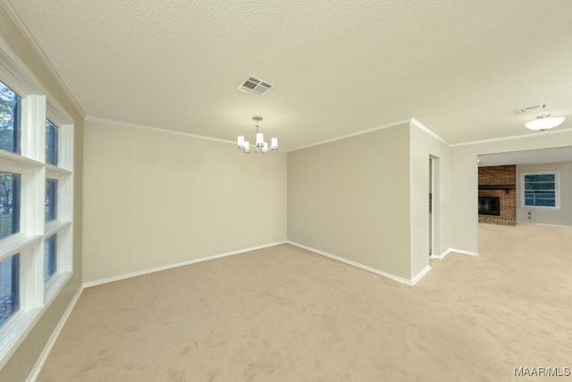 carpeted spare room with a textured ceiling, an inviting chandelier, a brick fireplace, and ornamental molding