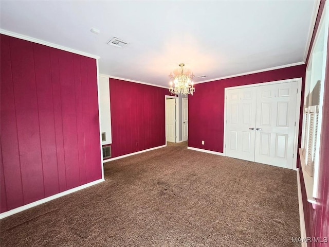 unfurnished bedroom with ornamental molding, a closet, a chandelier, and dark carpet