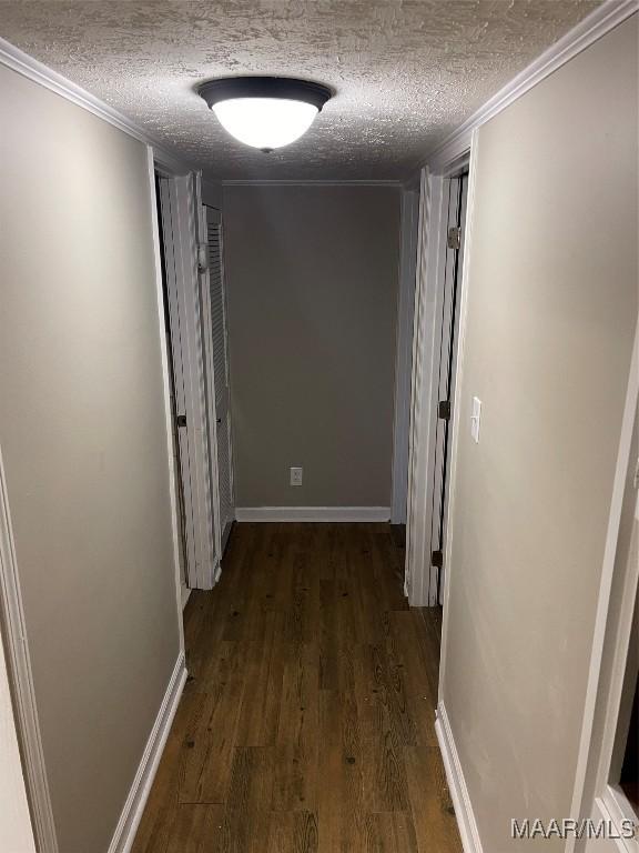 hallway with dark wood-type flooring, a textured ceiling, and ornamental molding