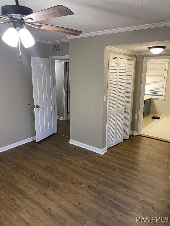 unfurnished bedroom with ceiling fan, crown molding, dark wood-type flooring, and a textured ceiling