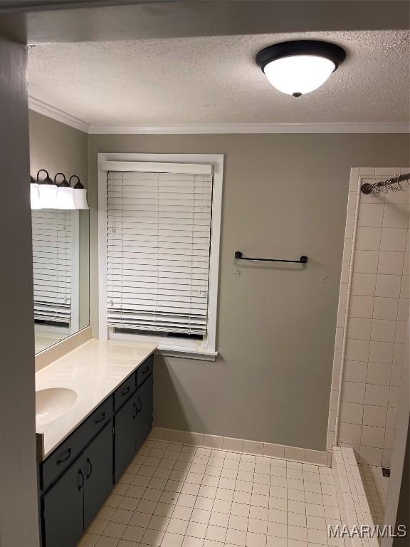 bathroom with a textured ceiling, vanity, a tile shower, and crown molding