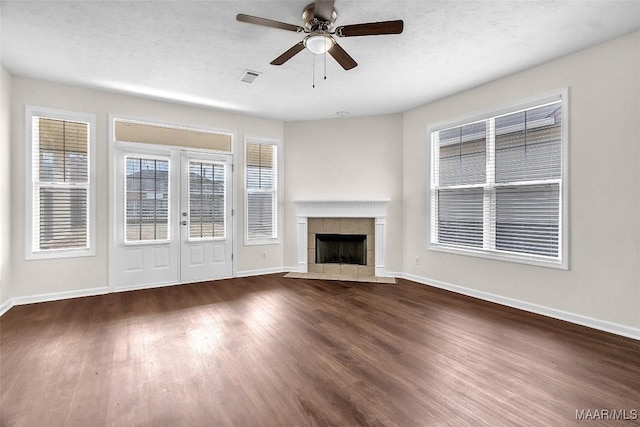 unfurnished living room with a tile fireplace, a textured ceiling, dark hardwood / wood-style floors, and ceiling fan