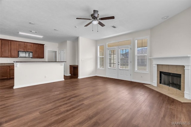 unfurnished living room featuring ceiling fan, dark hardwood / wood-style flooring, and a tile fireplace