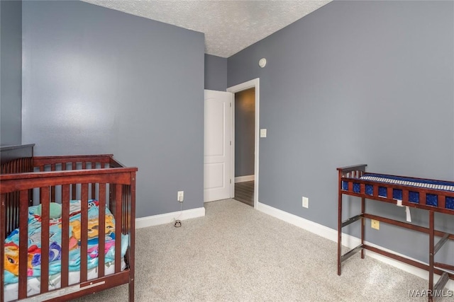 bedroom featuring a crib, a textured ceiling, and light colored carpet