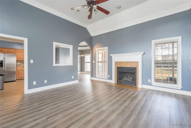 unfurnished living room with lofted ceiling, ceiling fan with notable chandelier, light hardwood / wood-style flooring, ornamental molding, and a tiled fireplace