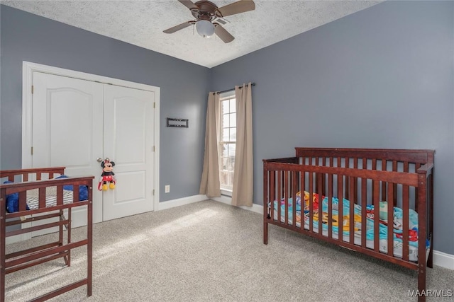 carpeted bedroom featuring a textured ceiling, a closet, a nursery area, and ceiling fan