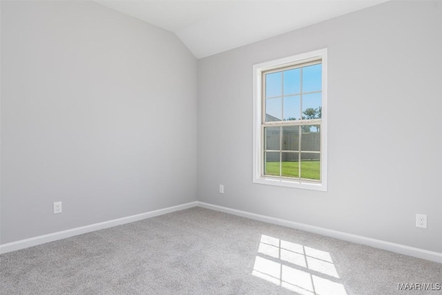 carpeted spare room featuring lofted ceiling and baseboards