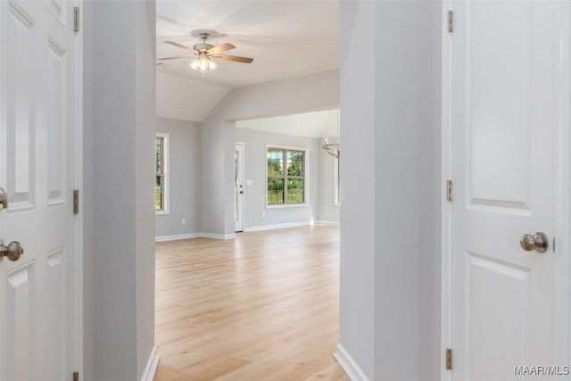 corridor featuring light wood-type flooring, lofted ceiling, and baseboards